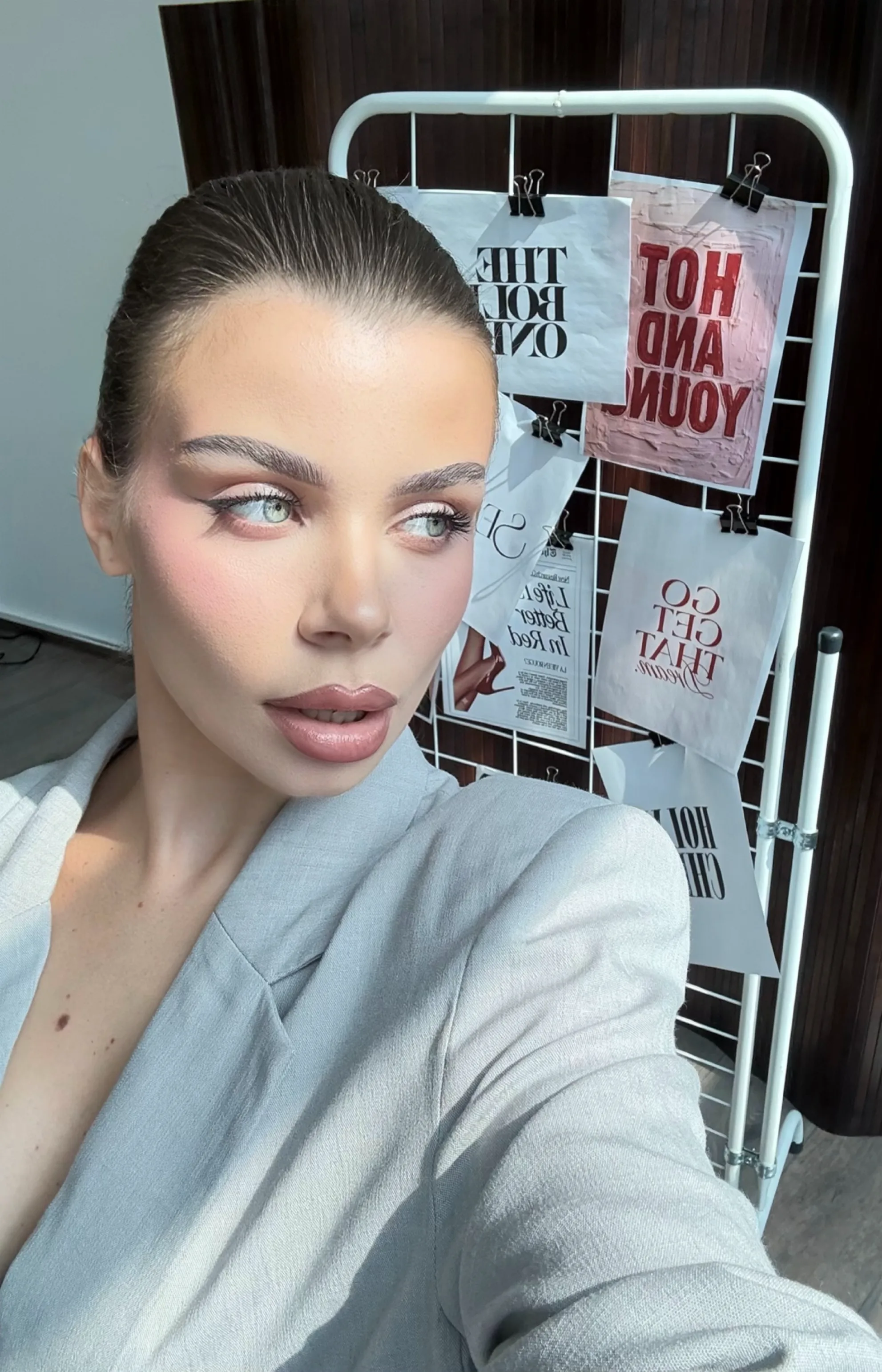 Clean daytime look on slicked-back hair — apricot blush drawn high on the cheek, brushed-up brows and a nude gloss.