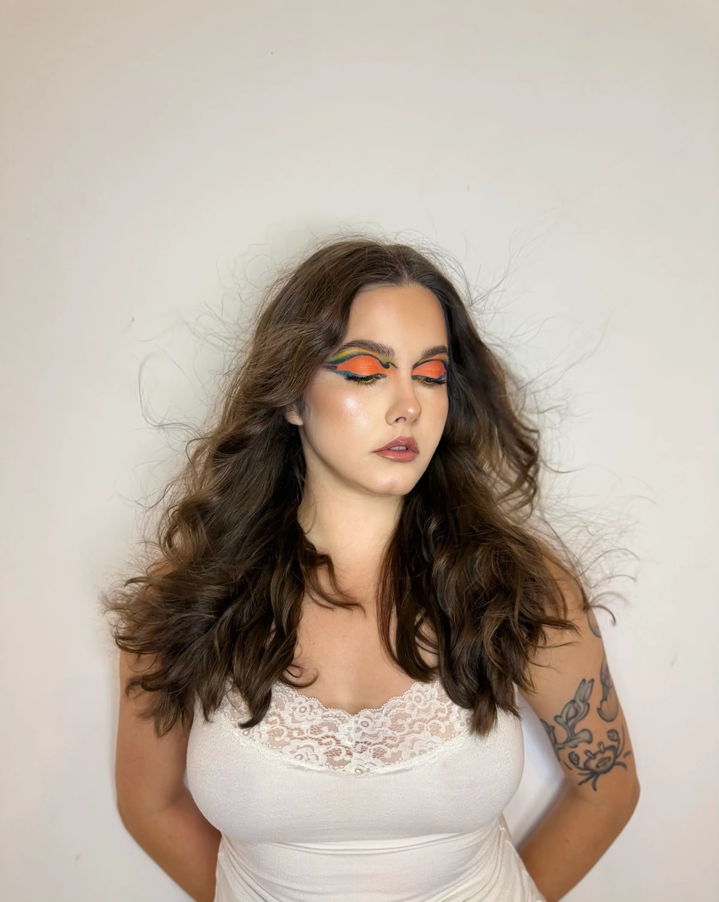 Full-length portrait of the rainbow liner look, hair in motion against a bare cream wall.